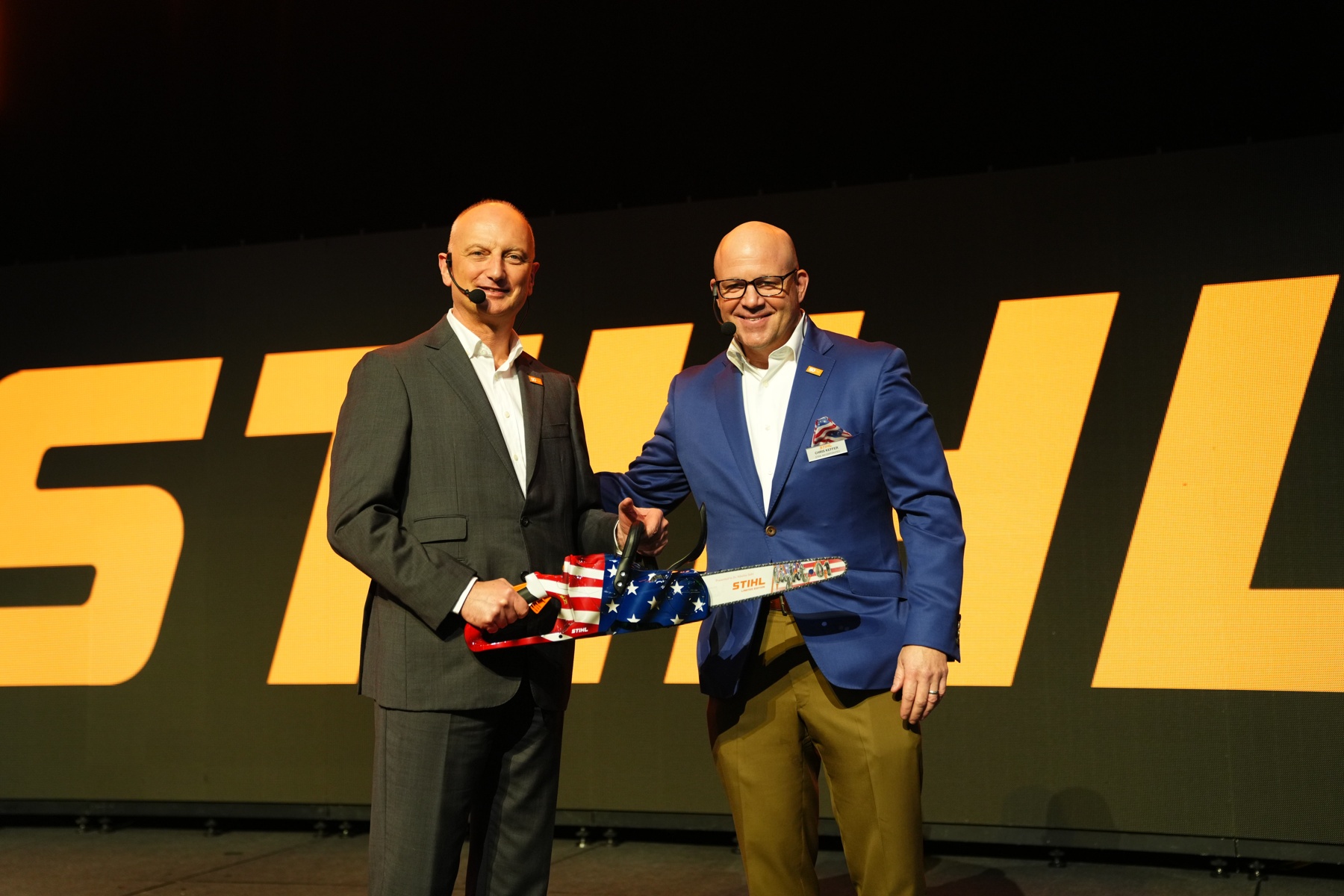 Dr. Nikolas Stihl (til venstre) og Chris Keffer, administrerende direktør for STIHL Inc. i USA, præsenterer en jubilæumssav med et amerikansk flag.